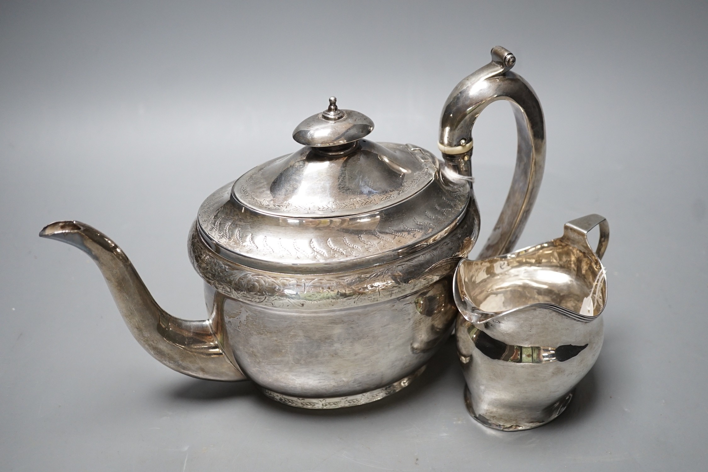 A George III engraved silver oval teapot on stand, Hannah Northcote? London, 1804 and Georgian silver cream jug, marks rubbed, gross 24.8oz.